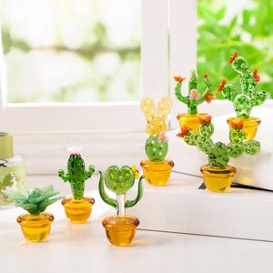 May include: A collection of miniature glass cactus sculptures in various shapes and sizes, each potted in a small yellow pot. The cacti are green with red and pink accents, and some have flower details.