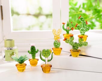 May include: A collection of miniature glass cactus sculptures in various shapes and sizes. Each cactus is a vibrant green with delicate details, set in small, yellow-orange pots. Some have pink or red flower accents.