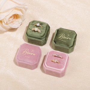 Könnte beinhalten: Zwei Ringboxen mit Samt-Innenausstattung. Eine Box ist grün mit goldenen Lettern, die "The Brown 01.13.23" sagen. Die andere Box ist rosa mit goldenen Lettern, die "The Brown 01.13.23" sagen. Beide Boxen enthalten Ringe.