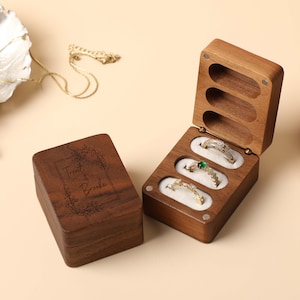 Könnte beinhalten: Eine Holzkiste mit drei Fächern für Ringe. Die Box ist mit dem Text "Trent & Brooke" und dem Datum "Oktober 2020" graviert.