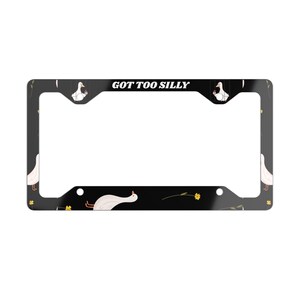 May include: Black license plate frame with a pattern of white geese and yellow flowers. The text "GOT TOO SILLY" is displayed at the top. The frame is designed to fit a standard U.S. license plate.