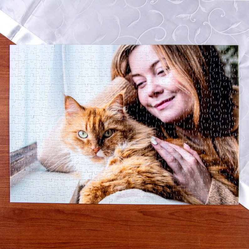 Peut inclure: Une femme aux longs cheveux bruns tient un chat roux. Le chat est couch&eacute; sur le c&ocirc;t&eacute; et regarde la cam&eacute;ra. La femme sourit et caresse le chat. L'arri&egrave;re-plan est un tissu &agrave; motifs blancs et bleus.