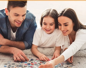 May include: A family of three, a man, a woman, and a young girl, are working together on a colorful jigsaw puzzle on the floor. They are all smiling and seem to be enjoying their time together.