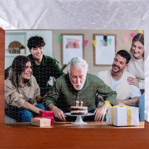 May include: A group of people celebrating a birthday with a cake and candles. The person in the center is blowing out the candles on a chocolate cake with white frosting. There are three candles on the cake. The people in the background are smiling and looking at the person blowing out the candles.