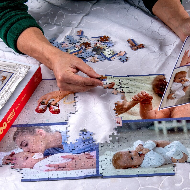 May include: A person is putting together a jigsaw puzzle with a baby theme. The puzzle pieces are on a white tablecloth. The puzzle shows images of babies, including a baby wearing a blue shirt and a baby wearing a white shirt. The puzzle box is red and white and says "500 Pieces 34cm x 46cm".