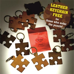 May include: A set of brown leather puzzle piece keychains with gold rings. The keychains are arranged on a white surface with a red pouch that says "for you from" in white text. The text "LEATHER KEYCHAIN FREE for those who order the puzzle!" is in a yellow circle on a brown background.