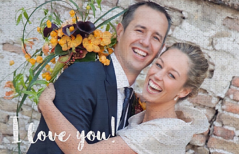 May include: A couple smiles and hugs in front of a brick wall. The woman is holding a bouquet of yellow and orange flowers. The text "I love you!" is written in white on the bottom of the image.