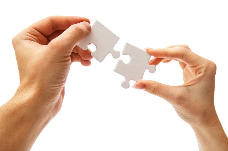 May include: Two hands holding two white puzzle pieces that fit together. The pieces are being held up to show how they fit together.