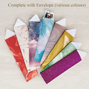 Op de afbeelding: Een verzameling kleurrijke, decoratieve enveloppen met witte driehoekige sluitingen. De enveloppen hebben verschillende patronen, waaronder marmer, glitter en hemelse ontwerpen. E&eacute;n envelop heeft een blauwe kwast en een kleine foto. De tekst bovenaan luidt "Complete with Envelope (various colours)".