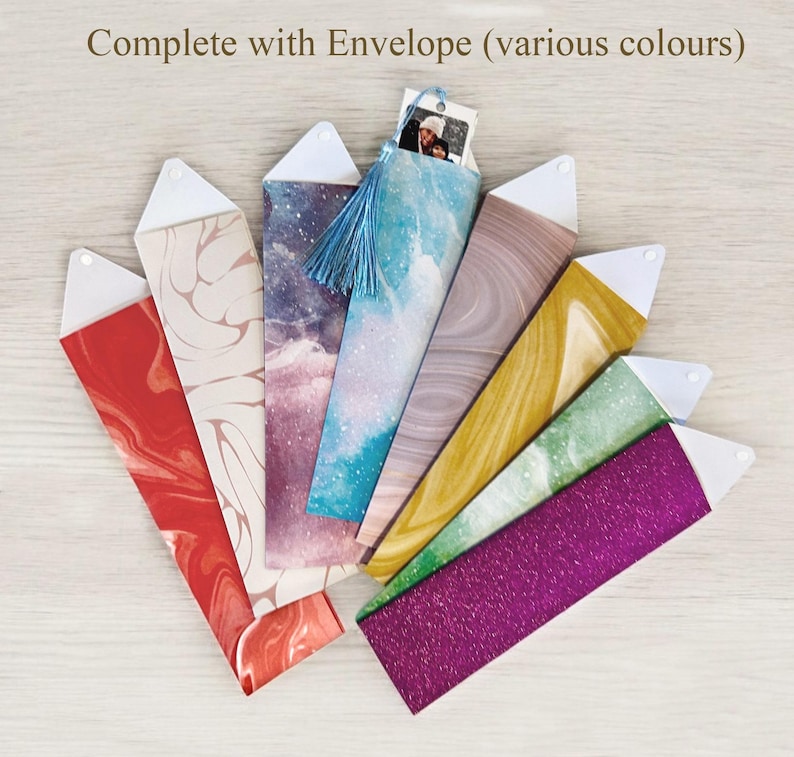 Op de afbeelding: Een verzameling kleurrijke, decoratieve enveloppen met witte driehoekige sluitingen. De enveloppen hebben verschillende patronen, waaronder marmer, glitter en hemelse ontwerpen. E&eacute;n envelop heeft een blauwe kwast en een kleine foto. De tekst bovenaan luidt "Complete with Envelope (various colours)".