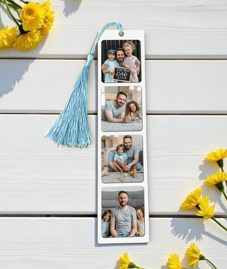 Op de afbeelding: Een witte boekenlegger met vier fotokaders, elk met een familiefoto. De boekenlegger heeft een lichtblauwe kwast en een klein gaatje aan de bovenkant. De bovenste foto bevat de tekst "THE BEST DAD EVER". Gele bloemen zijn op de achtergrond.