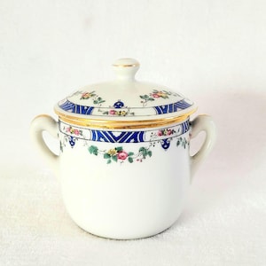 May include: A white porcelain sugar bowl with a lid, decorated with blue and gold floral patterns. The lid has a gold trim and a floral design.