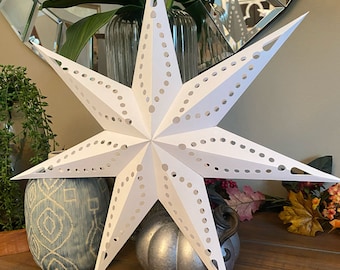 May include: A white paper star lantern with a decorative cut-out design. The star is hanging from the ceiling and is illuminated from within.