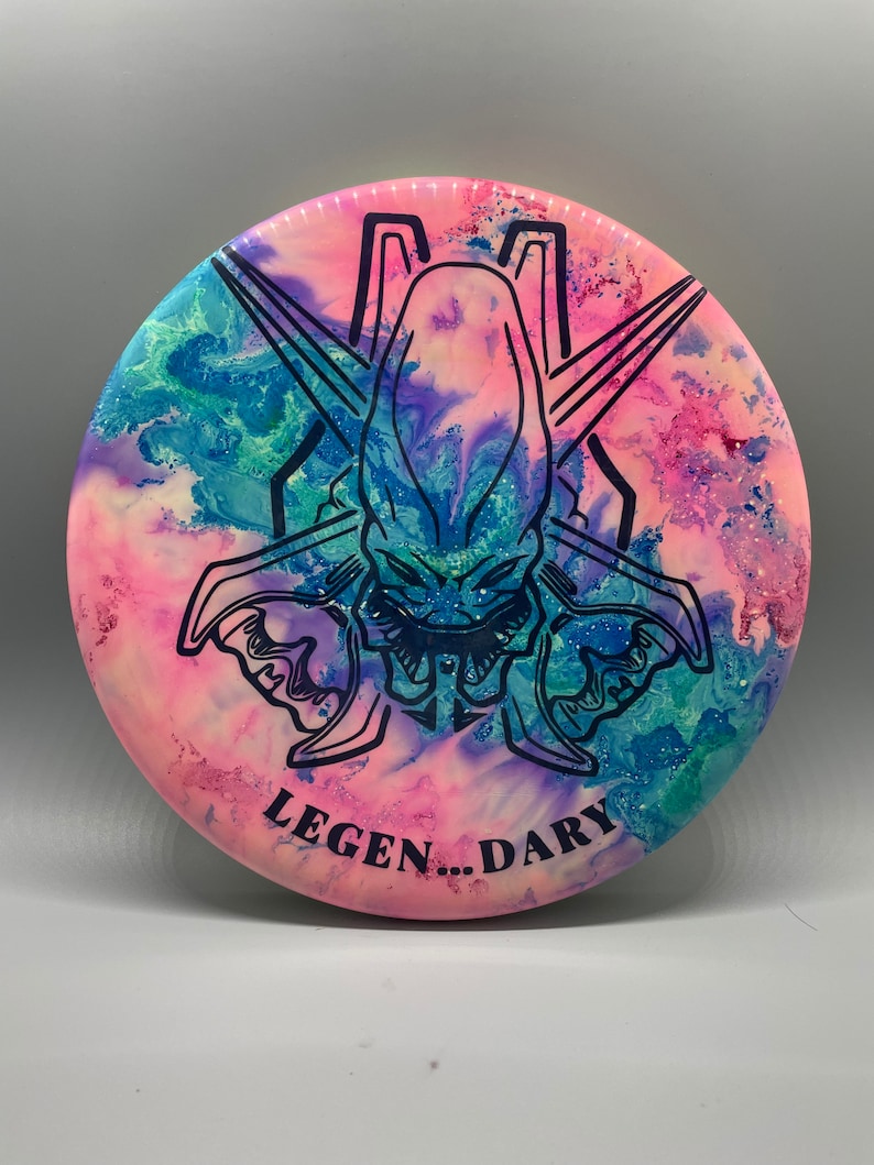 May include: A pink, blue, and green disc with a black alien-like creature graphic and the text "LEGEN...DARY".