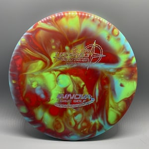 May include: A red, yellow, and blue disc golf disc with a swirl pattern. The disc has the text "The Star Destroyer" and "Speed 7, Glide 5, Turn 0, Fade 2" printed on it. The disc is made by Innova Disc Golf.