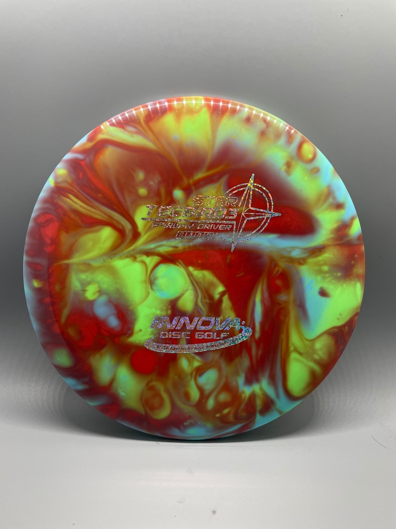 May include: A red, yellow, and blue disc golf disc with a swirl pattern. The disc has the text "The Star Destroyer" and "Speed 7, Glide 5, Turn 0, Fade 2" printed on it. The disc is made by Innova Disc Golf.
