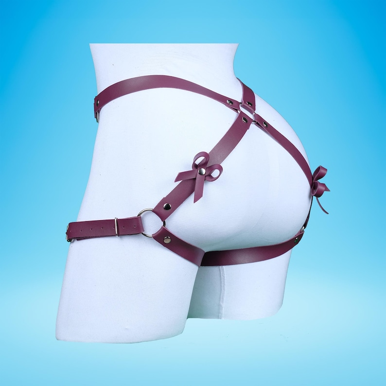 May include: Burgundy leather harness with two bows on the straps. The harness is designed to be worn around the hips and thighs.