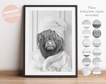 May include: Black and white photograph of a Highland cow wearing a white bathrobe and a towel on its head. The cow is looking at the camera. The photo is framed in a black frame. The text "More bathroom styles available" is written in black text on a white background.