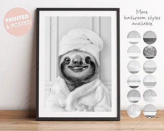May include: A black and white photograph of a sloth wearing a white bathrobe and a white towel on its head. The sloth is smiling and looking at the camera. The background is a white wall with white trim.