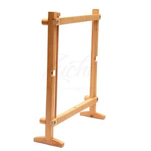 May include: A wooden weaving loom with a rectangular frame. The loom is made of light-coloured wood and features a series of notches along the top and bottom bars. The frame is supported by two vertical posts and two feet.