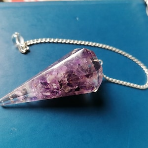 Könnte beinhalten: Ein violetter Amethyst-Kristall-Pendel mit einer silbernen Kette. Der Kristall ist klar und hat eine facettierte Form.
