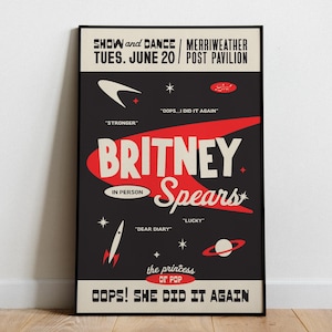 Puede incluir: Un póster enmarcado con fondo negro presenta el nombre "Britney Spears" en texto grande rojo y blanco. El póster incluye el texto "Show and Dance" y "Oops! She Did It Again", junto con otros detalles sobre un concierto.