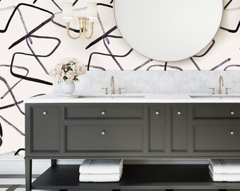 May include: A modern bathroom vanity with a large round mirror and a black and white patterned floor. The vanity is dark gray with gold hardware and a white countertop. A vase of flowers sits on the counter, and the wallpaper has a black abstract design.