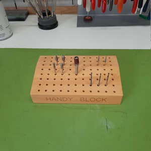 Peut inclure: Un bloc de bois avec des trous pour ranger de petits outils. Le bloc est étiqueté "HANDY-BLOCK".