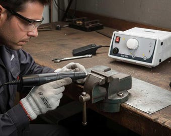 May include: A person using a black and gray rotary tool on a metal sheet secured in a vise. A white control box with the text "ECO 400" and a foot pedal are visible on the workbench. The person is wearing safety glasses and gloves.