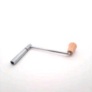 Könnte beinhalten: Ein silberfarbener Aufziehschlüssel mit einem Holzgriff. Der Schlüssel wird zum Aufziehen von mechanischen Uhren verwendet.
