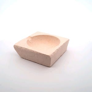 Op de afbeelding: Een vierkante, lichtroze keramische smeltkroes met een rond, verzonken midden. De smeltkroes is ontworpen voor het smelten van metaal.