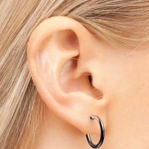 Könnte beinhalten: Nahaufnahme eines Ohrs mit einem kleinen, silbernen Creolenohrring. Der Ohrring ist schlicht und unaufdringlich und eine beliebte Wahl für Männer und Frauen.