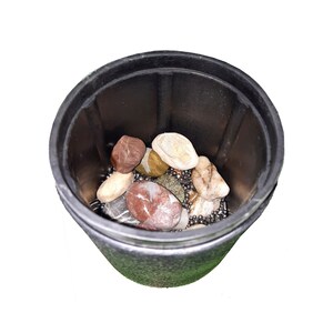 Puede incluir: Un recipiente de pl&aacute;stico negro lleno de peque&ntilde;as cuentas met&aacute;licas redondas, lisas y plateadas, as&iacute; como piedras de varios colores. Las piedras son marrones, rojas y blancas.