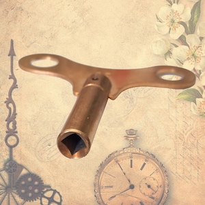 Puede incluir: Una llave de cuerda de reloj de latón con un mango de tres puntas y un eje de cuerda cuadrado. La llave está sobre un fondo vintage con un reloj de bolsillo.