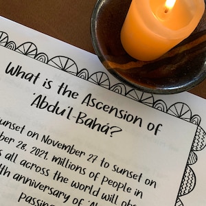 May include: A burning yellow candle in a small, dark brown ceramic bowl. A printed paper with the text "What is the Ascension of 'Abdu'l-Bahá?" is in the foreground. The paper has a decorative border.