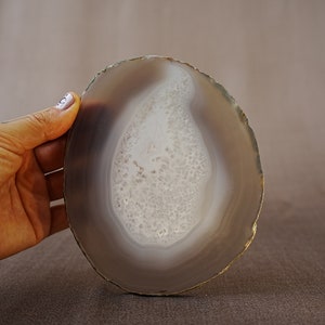 May include: A round, grey agate slice with a white, banded pattern in the centre. The agate is smooth and polished.