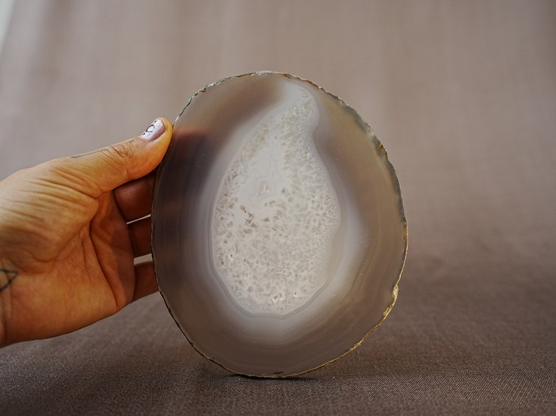 May include: A round, grey agate slice with a white, banded pattern in the centre. The agate is smooth and polished.