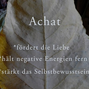 May include: A close-up of a dried leaf with the word "Achat" written on it. The leaf is a light brown colour with a yellow tint. The text on the leaf reads: *"f&ouml;rdert die Liebe" *"h&auml;lt negative Energien fern" *"st&auml;rkt das Selbstbewusstsein"