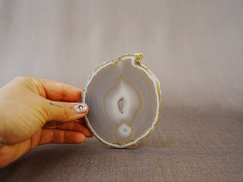 May include: A light grey agate slice with a white centre and brown edges. The agate is translucent and has a natural, organic shape.