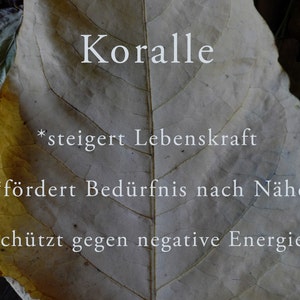 May include: A close-up of a leaf with the word "Koralle" written on it. The leaf is a light brown colour with a yellow tint. The text below the word "Koralle" reads: *steigert Lebenskraft *f&ouml;rdert Bed&uuml;rfnis nach N&auml;he *sch&uuml;tzt gegen negative Energien