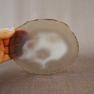 May include: A round, grey agate slice with a white centre and brown edges. The agate has a natural, organic shape and is perfect for use as a coaster or decorative piece.