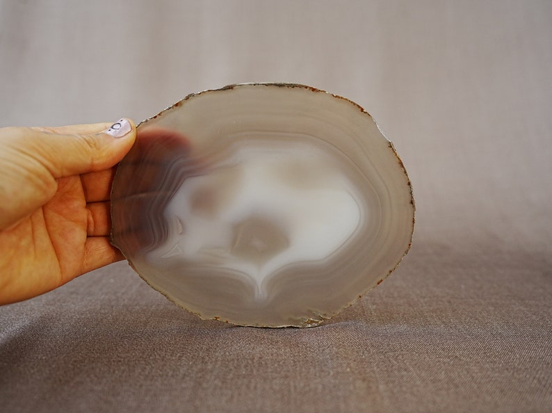 May include: A round, grey agate slice with a white centre and brown edges. The agate has a natural, organic shape and is perfect for use as a coaster or decorative piece.