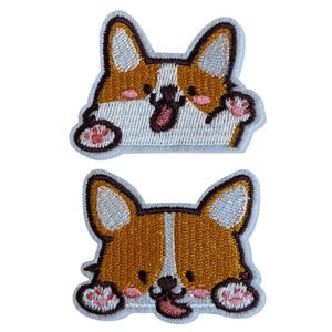 May include: Two embroidered patches of a cartoon corgi dog with brown and white fur. The corgi is smiling with its tongue sticking out. One patch has the corgi waving its paw. The other patch has the corgi with its paws on the bottom of the patch.