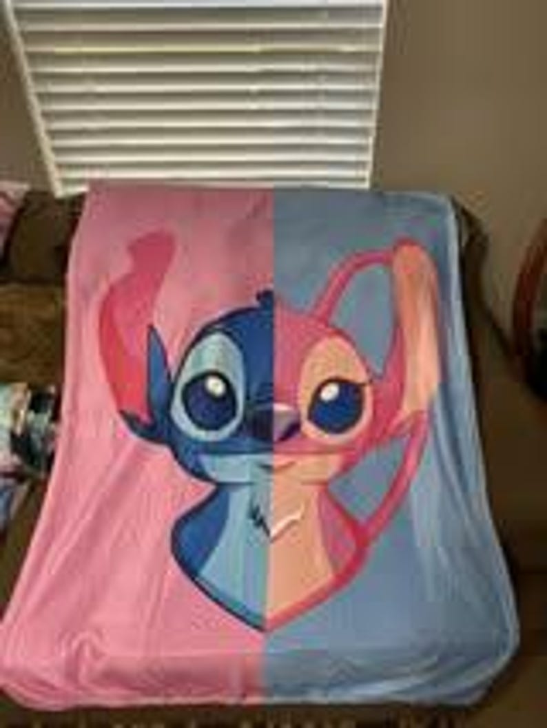 Może przedstawiać: Koc z polaru z podzielonym wzorem z postaciami Stitch i Angel z filmu animowanego Lilo & Stitch. Lewa strona jest r&oacute;żowa ze Stitchem, a prawa strona jest niebieska z Angel.