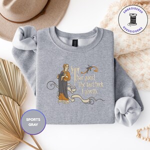 Puede incluir: Una sudadera gris deportivo de cuello redondo con un bordado que muestra una figura de estilo medieval con t&uacute;nica oscura. El texto dice "Thar goes! The last fvck I giveth." El dise&ntilde;o incluye volutas decorativas y un peque&ntilde;o p&aacute;jaro.