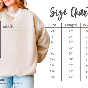 Pu&ograve; includere: Una felpa beige a girocollo con una tabella delle taglie che mostra le misure in pollici dalla XS alla 5XL. La tabella include colonne per lunghezza e larghezza, con frecce sulla felpa che indicano dove vengono prese le misure.