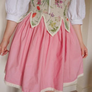 May include: A pink dress with a floral bodice and a full skirt. The bodice has a cream fabric with a colourful floral print. The skirt is solid pink with a lace trim at the hem. The dress has white sleeves.