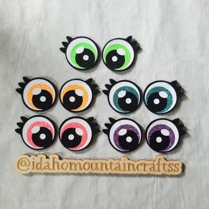 May include: Set of ten felt googly eyes with glitter accents in various colors, including green, orange, teal, pink, and purple. The eyes are approximately 1 inch in diameter.  @idaho mountaincraftss