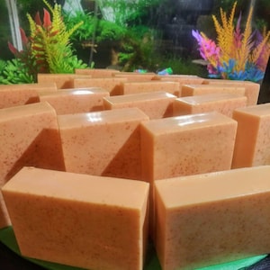 May include: A close-up of a group of orange-colored soap bars arranged in rows. The bars have a grainy texture and are displayed on a green surface.