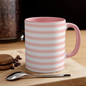 May include: A pink ceramic mug with a white and pink striped pattern. The mug has a pink interior and a handle.